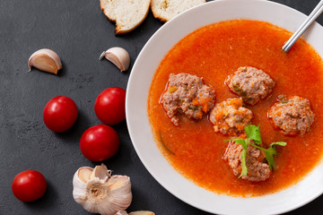 plate of red tomato soup with meatballs, garlic and cilantro on a black background top view, fresh cherry