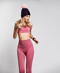 Obraz na płótnie Canvas Beautiful blonde woman with perfect athletic slim figure by physical education or fitness, leads a healthy lifestyle, wears comfortable pink casual clothes in the style of sports. warm hat with pompon