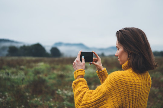 photographer girl hold in hands mobile phone taking photo on smartphone autumn foggy mountain, tourist shooting on photo camera on background landscape, hobby concept