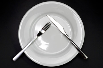 Table setting. Empty plate, knife and fork on a black background. Fork and knife are on the plate, pause in food. Top view and flat lay with copy space.