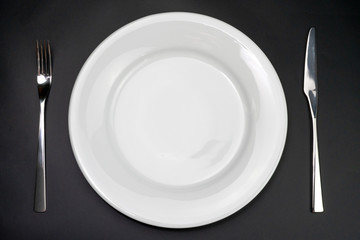 Table setting. Empty plate, knife and fork on a black background. Top view and flat lay with copy space.