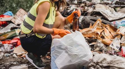 Woman volunteer helps clean the field of plastic garbage. Bushes and sky in the background. Earth day and ecology.
