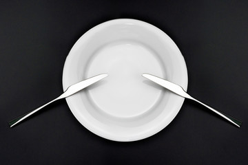 Table setting. Empty plate, two knives on a black background. Top view and flat lay with copy space.