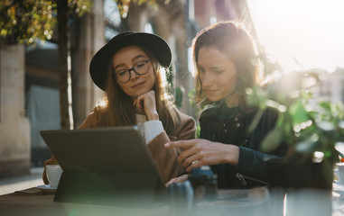 Friends using digital tablet together. Girls hipster travels in sun Barcelona sitting in cafe....