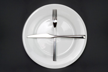 Table setting. Empty plate, knife and fork on a black background. A fork and a knife lie on a plate, waiting for the next dish. Top view and flat lay with copy space