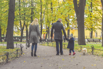 family mom dad and daughter walking in the Park with a dog