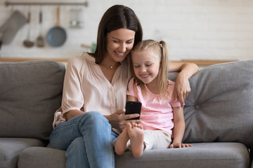 Happy young mother and little daughter using phone together