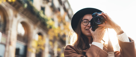 Photographer in glasses with retro photo camera. Tourist portrait girl in hat travels in Barcelona holiday. Sunlight flare street in europe city. Traveler hipster shoot architecture, copy space mockup