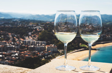 Two drink glass white wine standing on background blue sea top view city coast yacht from observation deck, romantic toast with alcohol panoramic cityscape downtown