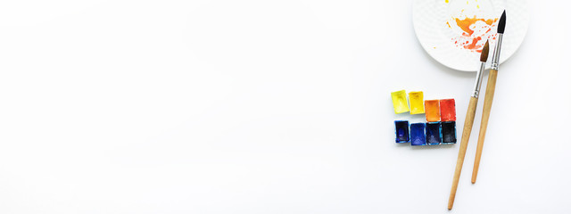 Watercolor, brushes and palette on a white background, top view. Hobbies and good mood