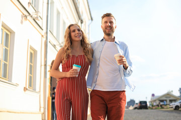 Obraz premium Beautiful young couple holding hands and smiling while walking through the city street