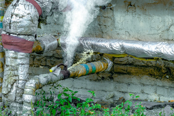 Damaged careless and unprofessionally insulated pipe with hot steam and dirty water splashing out of the damaged area