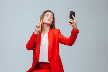 girl in a red jacket takes a selfie on the phone on a gray background