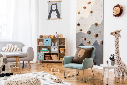 Stylish scandinavian interior design of childroom with gray sofa, modern climbing wall for kids, design furnitures, soft toys, teddy bear and cute children's accessories. Home decor. Template. 