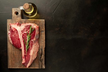 Raw t-bone steak with fresh herbs on a concrete or slate background, top view, place for text,