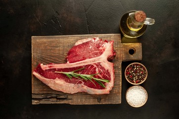 Raw t-bone steak with fresh herbs on a concrete or slate background, top view