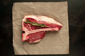 Raw t-bone steak with fresh herbs on a concrete or slate background, top view