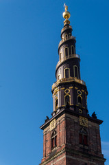 Fototapeta na wymiar Church of Our Saviour in Copenhagen, Denmark. The black and golden spire reaches a height of 90 metres and the external staircase turns four times counterclockwise around it