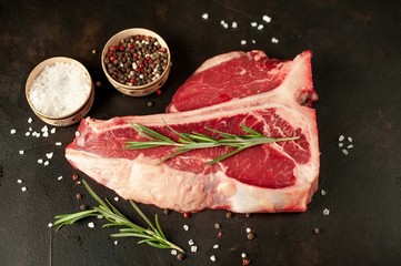 Fototapeta na wymiar Raw t-bone steak with fresh herbs on a concrete or slate background, top view