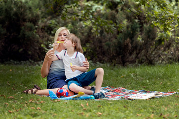 Mother and her impaired son blowing soap bubbles on a park lawn
