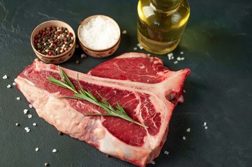 Raw t-bone steak with fresh herbs on a concrete or slate background, top view