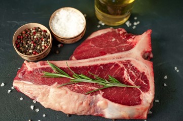 Raw t-bone steak with fresh herbs on a concrete or slate background, top view