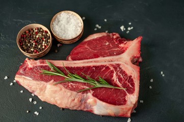 Raw t-bone steak with fresh herbs on a concrete or slate background, top view