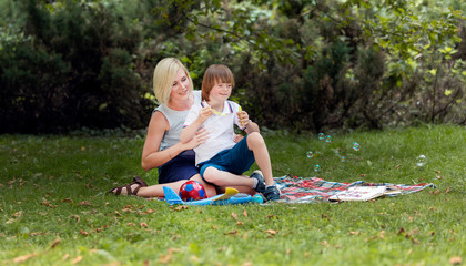 Special kid enjoys amusing himself with soap bubbles on a park lawn