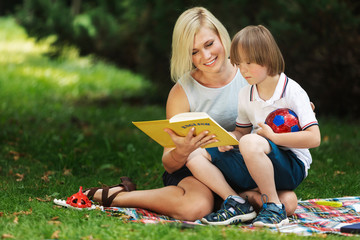 Affectionate mom reads a book to her special kid on a park lawn