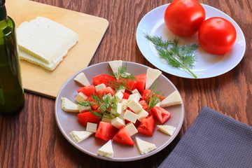 salad of tomatoes and Adyghe cheese. tomatoes and dill on a platter. slices of adyghe cheese on a cutting board. olive oil