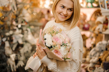 Smiling girl holding a bouquet of tender pink peony roses decorated with little branches and green leaves