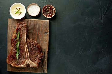 Grilled T-bone steak on a stone table. With rosemary and spices. Top view with copy space.