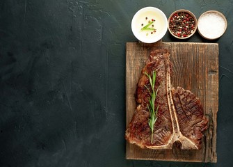 Grilled T-bone steak on a stone table. With rosemary and spices. Top view with copy space.