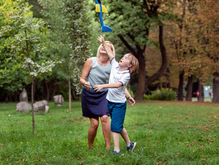 Special sunny kid and his loving mother launching a toy airplane on a park lawn