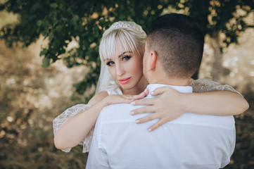 Beautiful blonde bride hugs the groom and looks out from behind. Wedding portrait of lovers newlyweds close-up. Photography and concept.