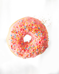 Pink donut with pastry topping and flying rainbow colored Sprinkles