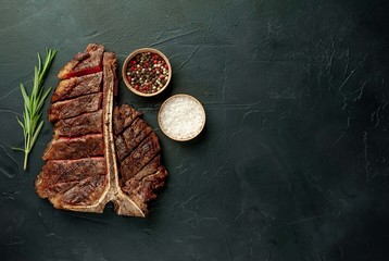 Fototapeta na wymiar Grilled T-bone steak on a stone table. With rosemary and spices. Top view with copy space.