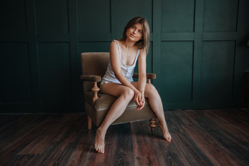 Obraz na płótnie Canvas Beautiful girl with long thin legs sitting on a chair on a dark green background