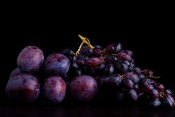 fresh blue plums and grapes on a black reflective background