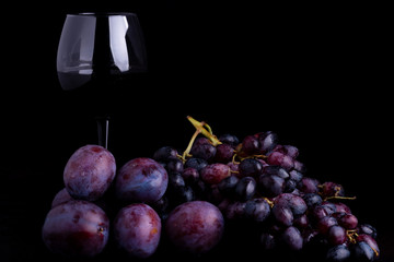 fresh blue plums, grapes and glass of wine on a black reflective background