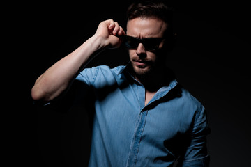 casual man standing and fixing sunglasses with strong attitude