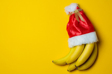 christmas bananas on yellow background in santa claus cap, holiday products concept