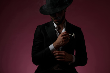 Mysterious man fixing his sleeve and smoking a cigarette