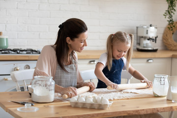 Happy mother and little daughter rolling out dough together