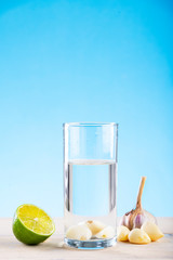 Head of garlic in a glass of water on a blue background with a slice of lemon, garlic water, lemon water, disease prevention