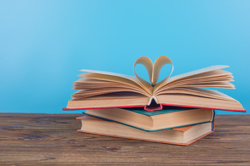 An open book lies on a wooden table. Pages are folded in a heart. The concept of love to read books, learning, study, school, education.