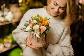 Smiling woman holding a peach color box with pink roses and yellow orchid decorated with fir-tree branches