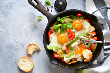 Fried eggs with vegetables in a pan on a gray concrete background. View from above.