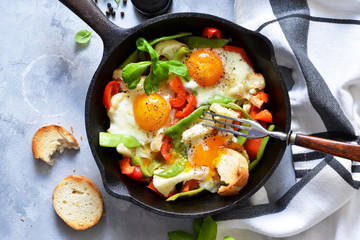 Fried eggs with vegetables in a pan on a gray concrete background. View from above.