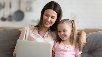 Smiling mother and little daughter using laptop together close up